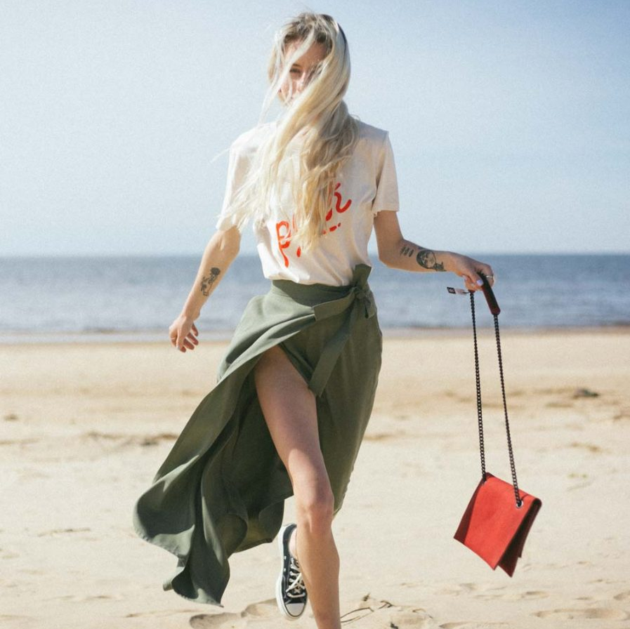 Stylish woman in summer outfit at the beach with red bag, available on USMIH Grid for card and cryptocurrency payments.