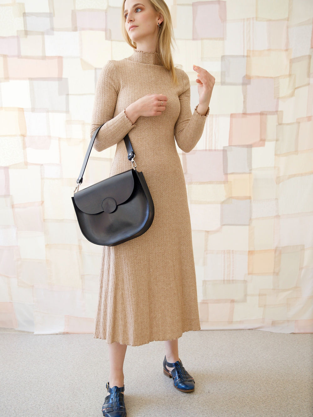 Woman holding black FIONA handbag with magnet closure, wearing a beige dress, ideal for a night out. Hand-made by TOKS VISOKS in Lithuania.