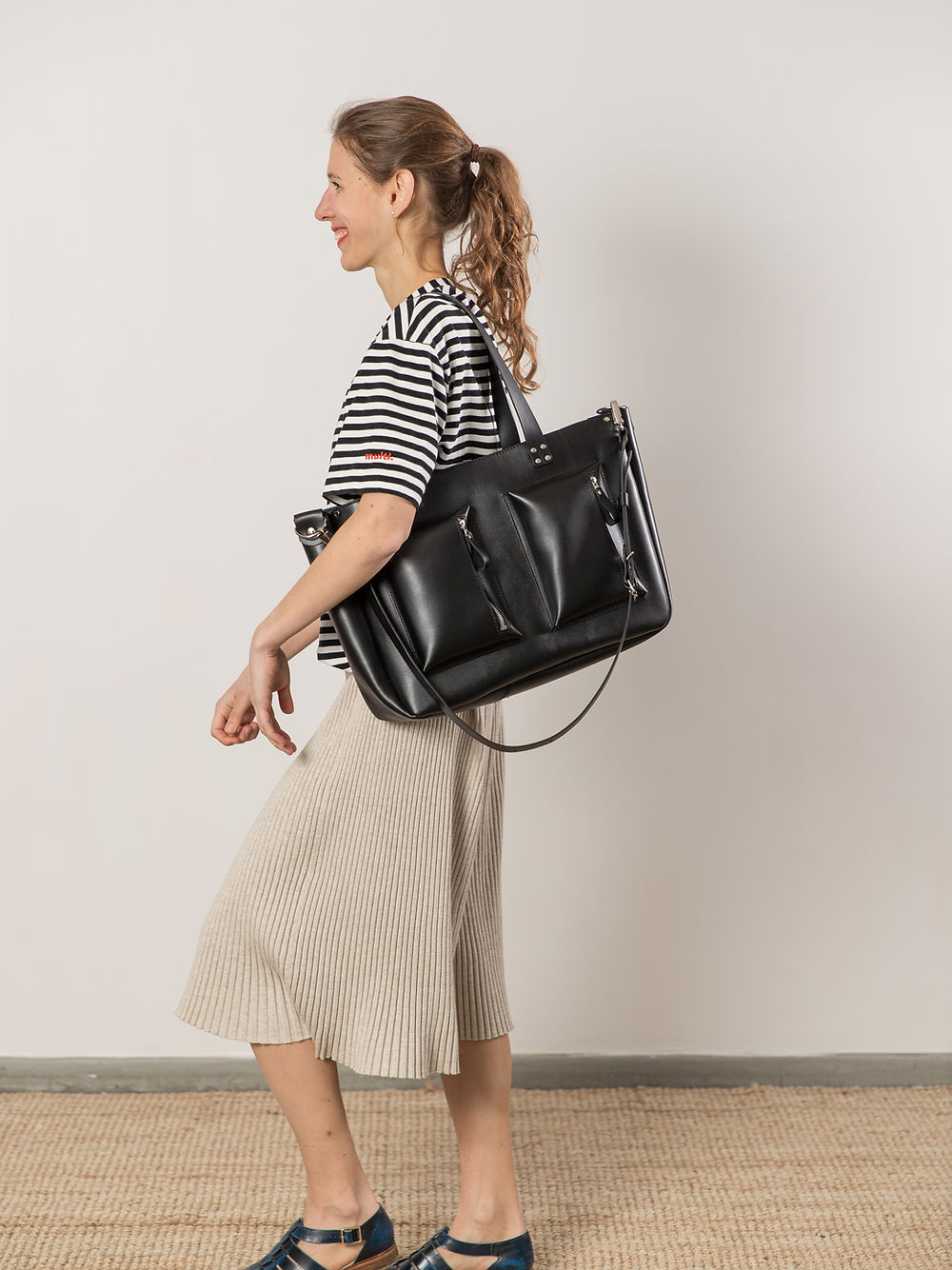 Woman carrying AMBER black handbag with USMIH Grid, showcasing spacious design, long handles, and elegant style.