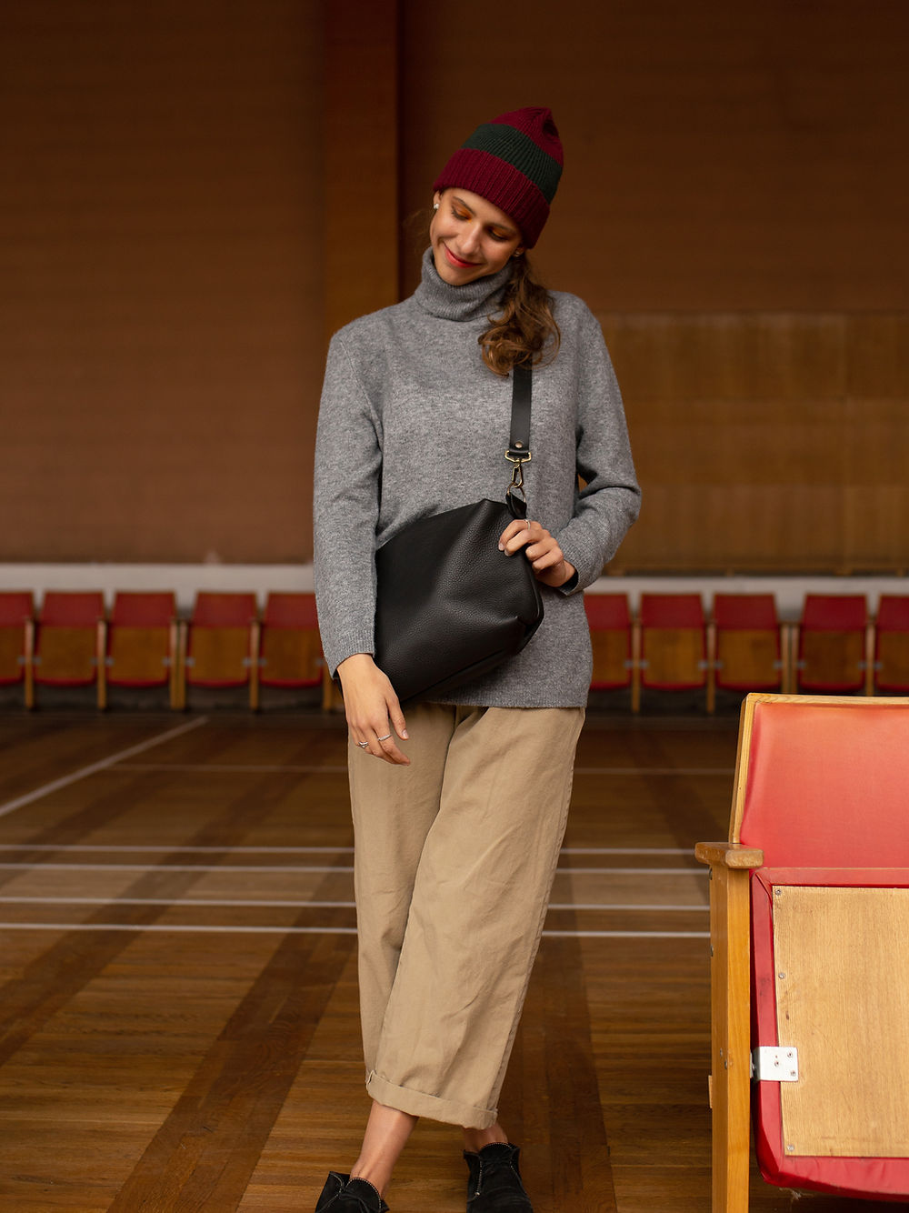 Woman wearing a grey sweater and beige pants, holding a ROBIN Leather Handbag Large in black, available on USMIH Grid for card and crypto payments.