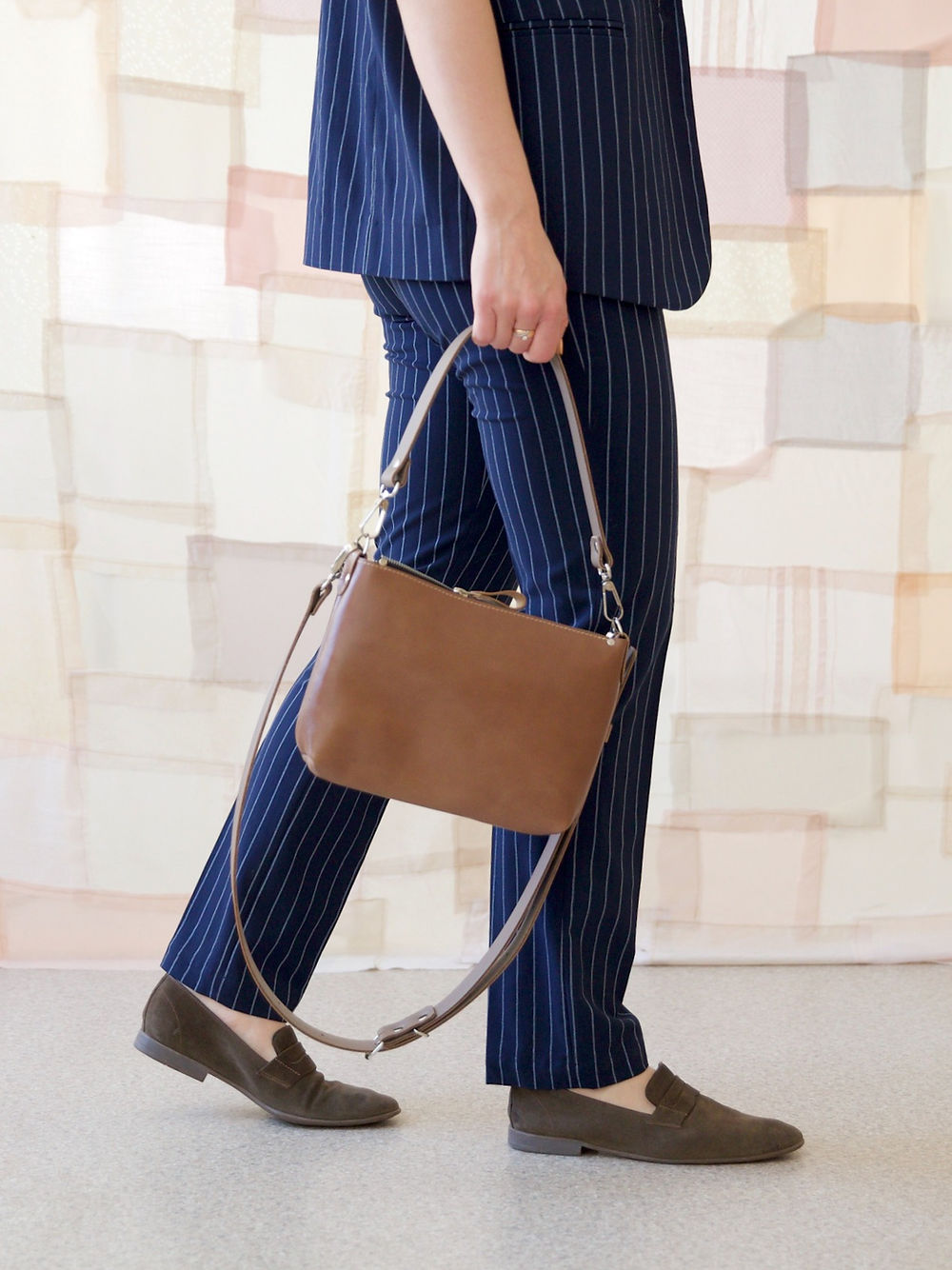 Person holding cappuccino TOMMY leather bag with adjustable handles, available on USMIH Grid, accepting card and cryptocurrency payments.