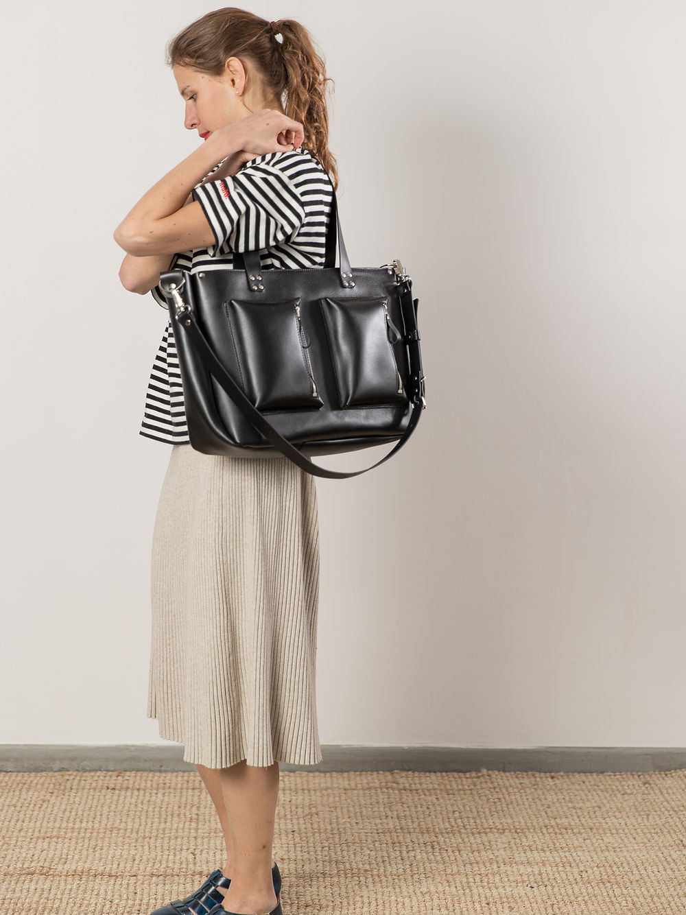 Woman carrying black AMBER handbag with USMIH Grid, showcasing spacious design with long handles and multiple pockets.