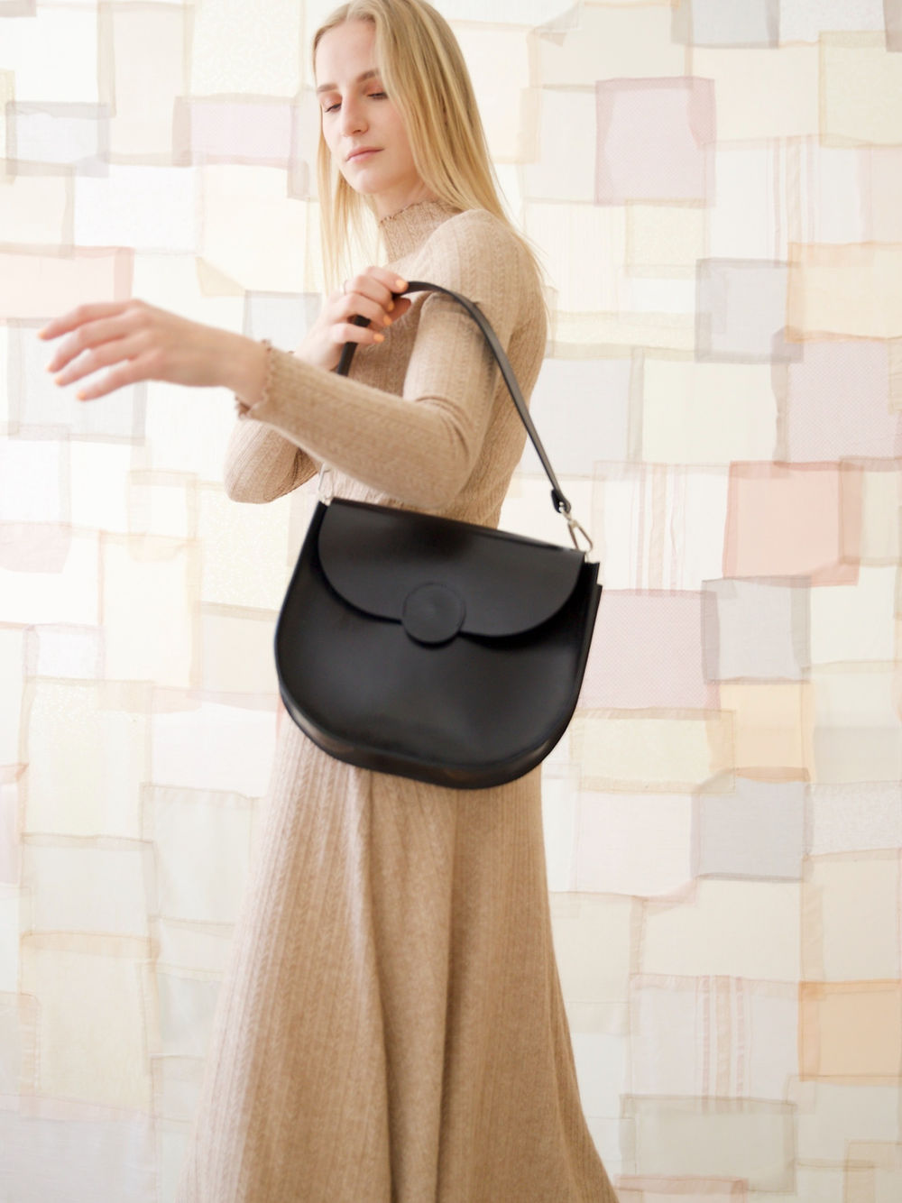 Woman holding a black FIONA handbag with magnet closure, perfect for city life and evening outings, hand-made in Lithuania by TOKS VISOKS.