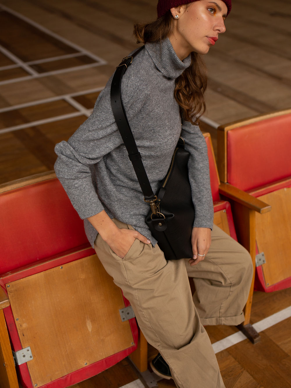 Woman sitting with ROBIN large black leather handbag in modern seating area, highlighting adjustable strap; available on USMIH Grid.