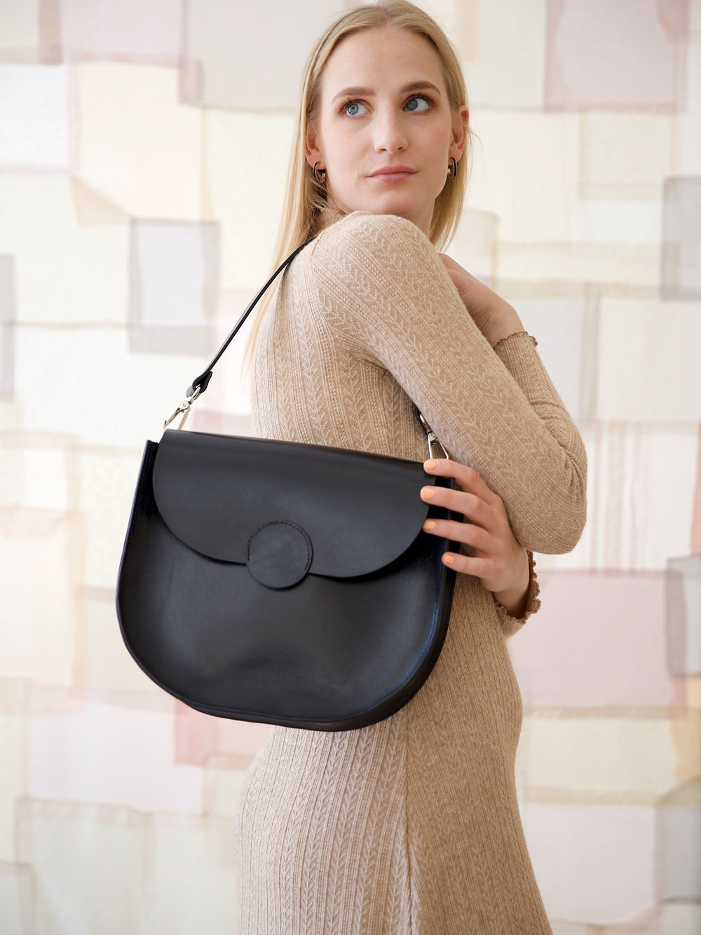 Woman holding black FIONA handbag with magnet closing and shoulder strap, perfect for city life or evening outings. Hand-made in Lithuania.