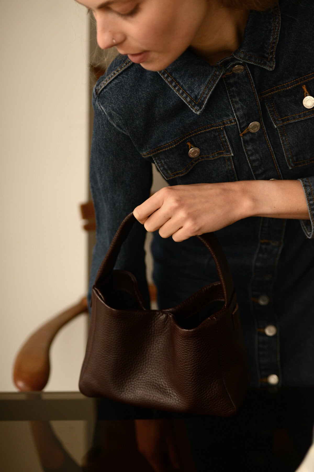 Woman holding a dark brown crossbody bag MERU, made from Italian vegetable tanned leather, showcasing its stylish design.