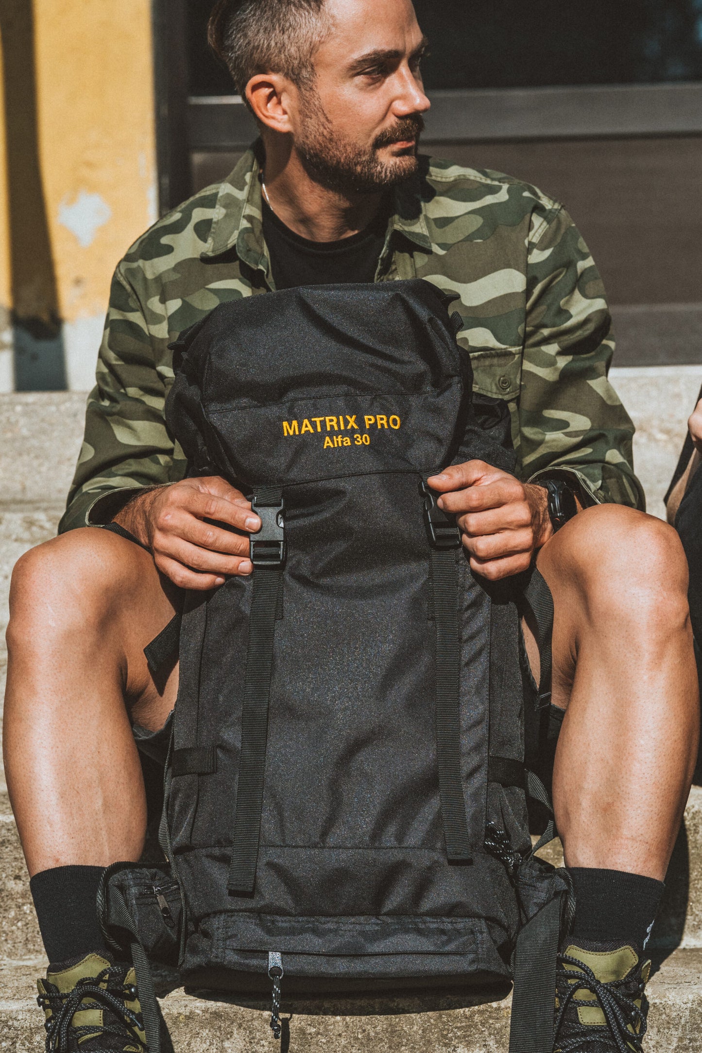 Man sitting with Alfa 30 Hiking Bag by Matrix Pro, featuring USMIH Grid, suitable for hiking and everyday use.