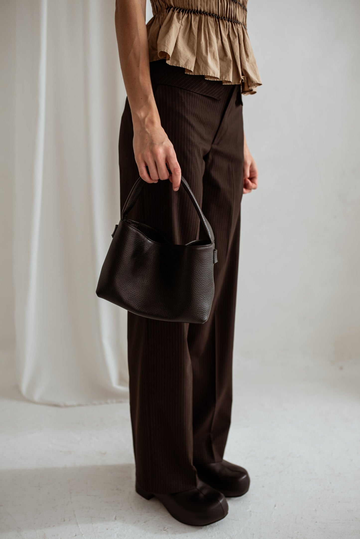 Person holding minimalist black crossbody bag Meru, featuring a short handle, made from high-quality Italian vegetable tanned leather.