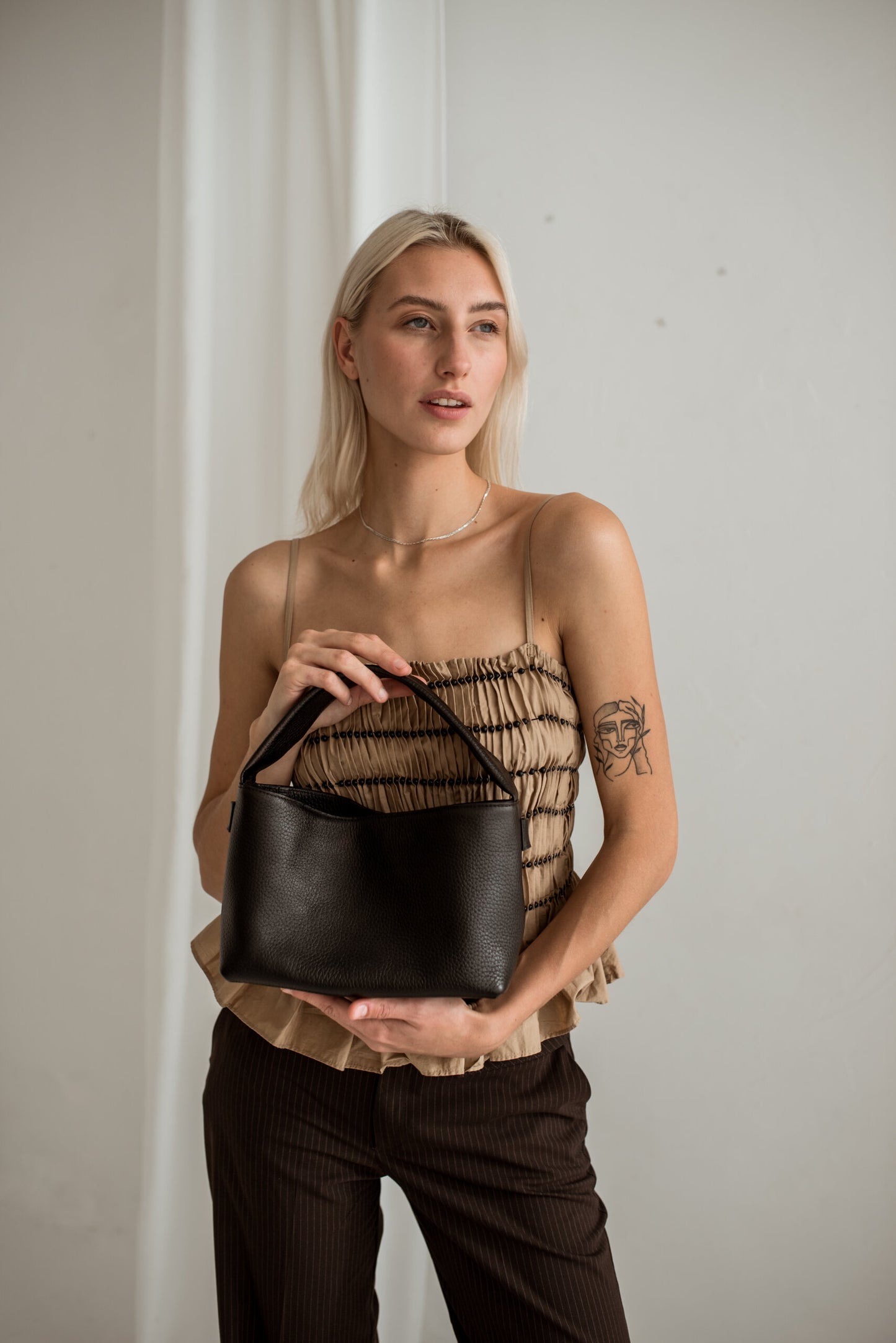 Woman holding a black Meru crossbody bag with adjustable strap, made from Italian vegetable tanned leather. Perfect luxury gift idea.