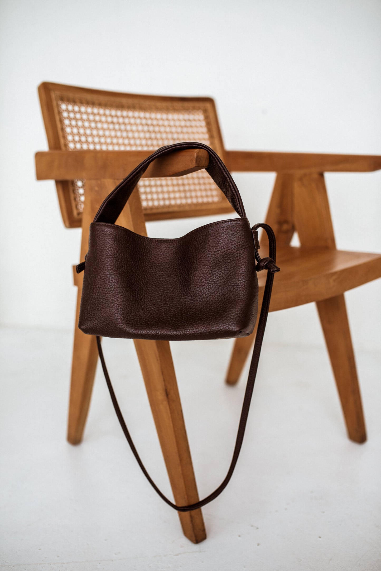 Dark brown minimalist crossbody bag Meru on a wooden chair, crafted from natural Italian leather, perfect luxury gift idea | Find USMIH.