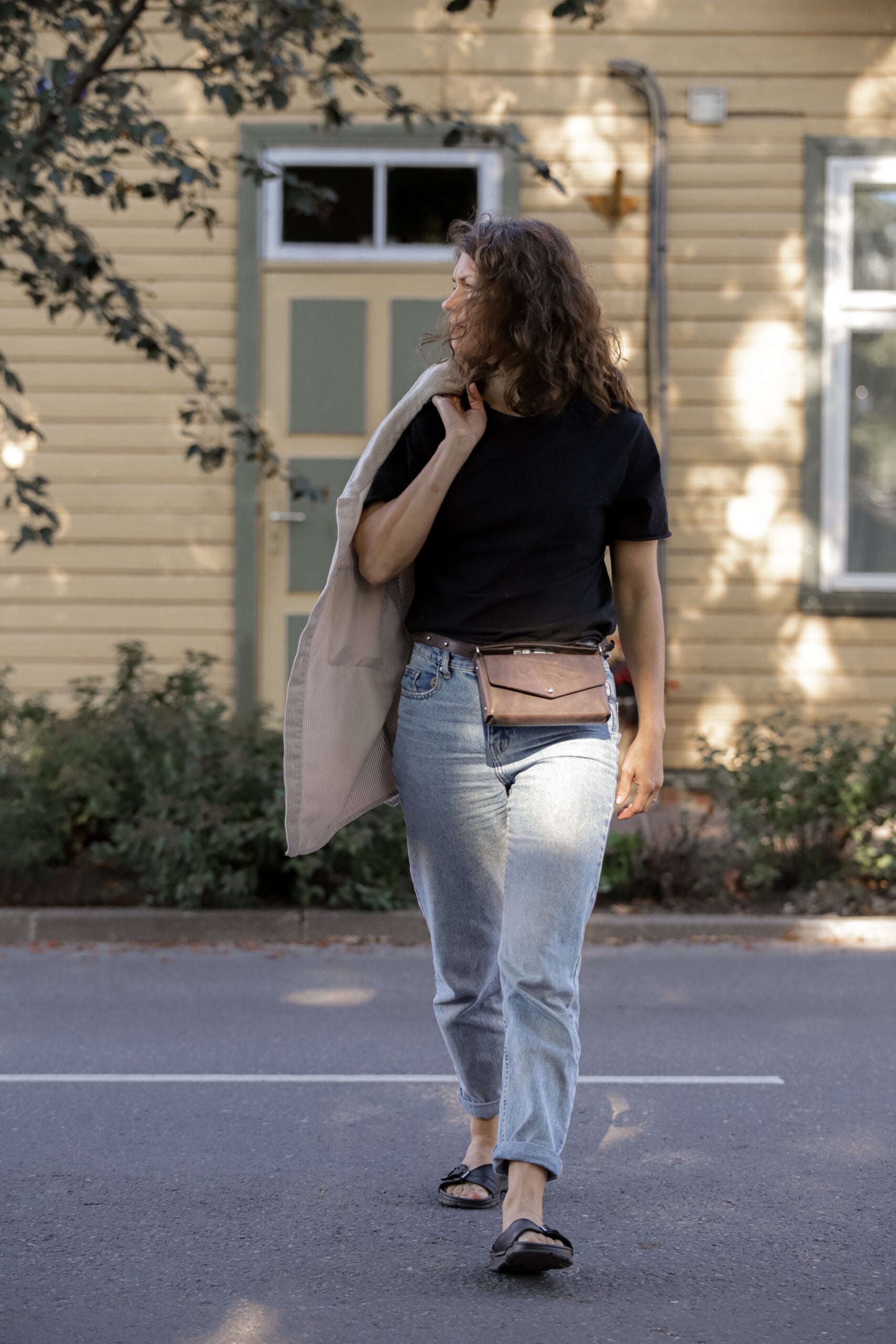 Woman wearing Crossbody Leather Bag KOKUKA, styled as a belt bag, walking outdoors in casual outfit.