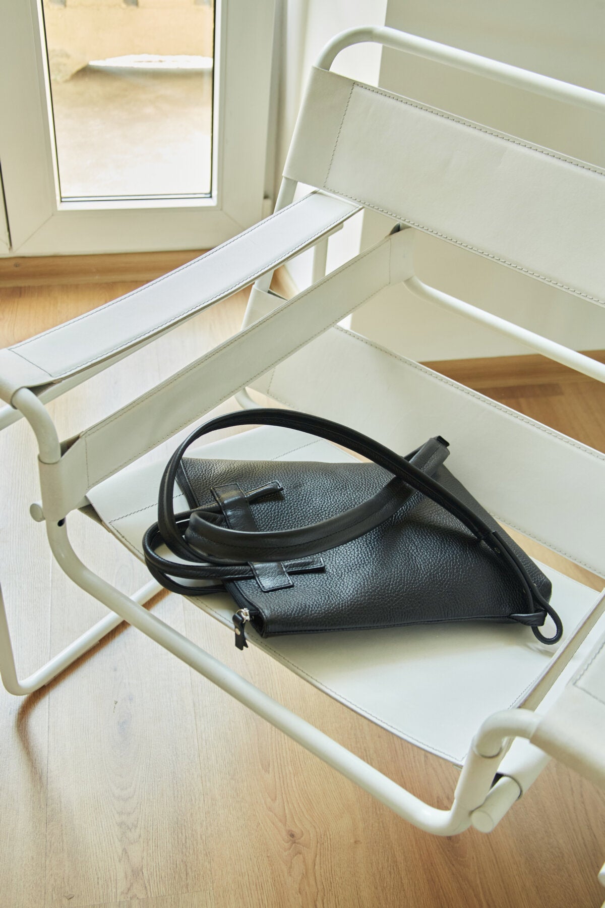 Minimalist leather backpack on chic white chair, featuring grain texture and knot design, perfect luxury gift idea.