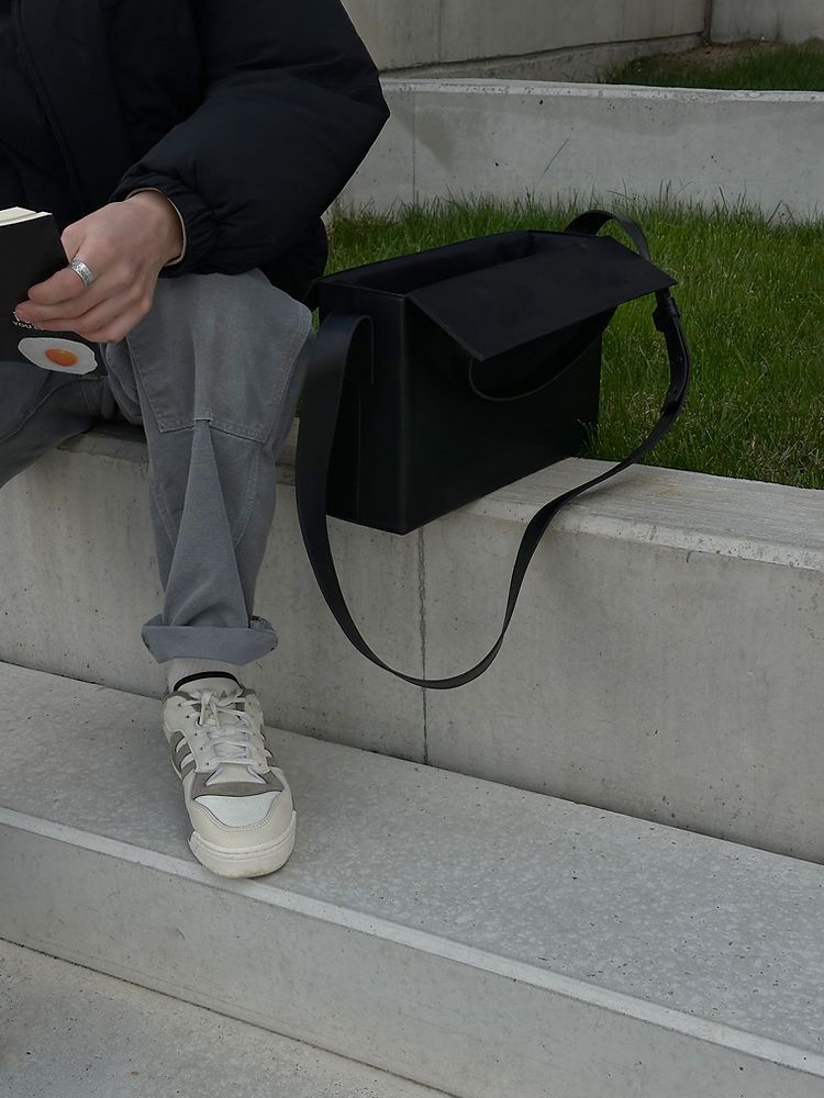 Person sitting on steps with a black leather BOX Bag featuring a sleek design, highlighting its simplicity and USMIH Grid elegance.