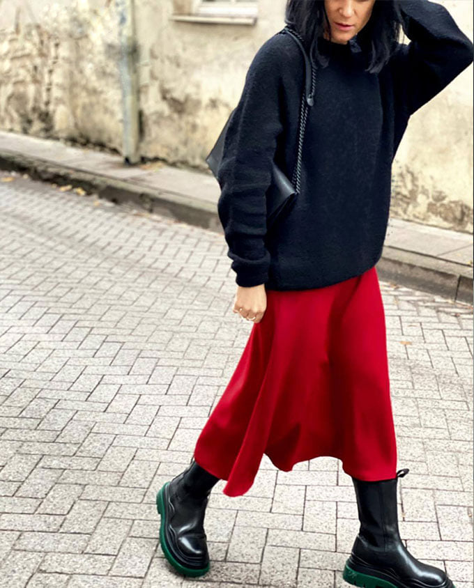 Woman wearing black sweater and red skirt with black Chain Shoulder Bag walking on cobblestone street.