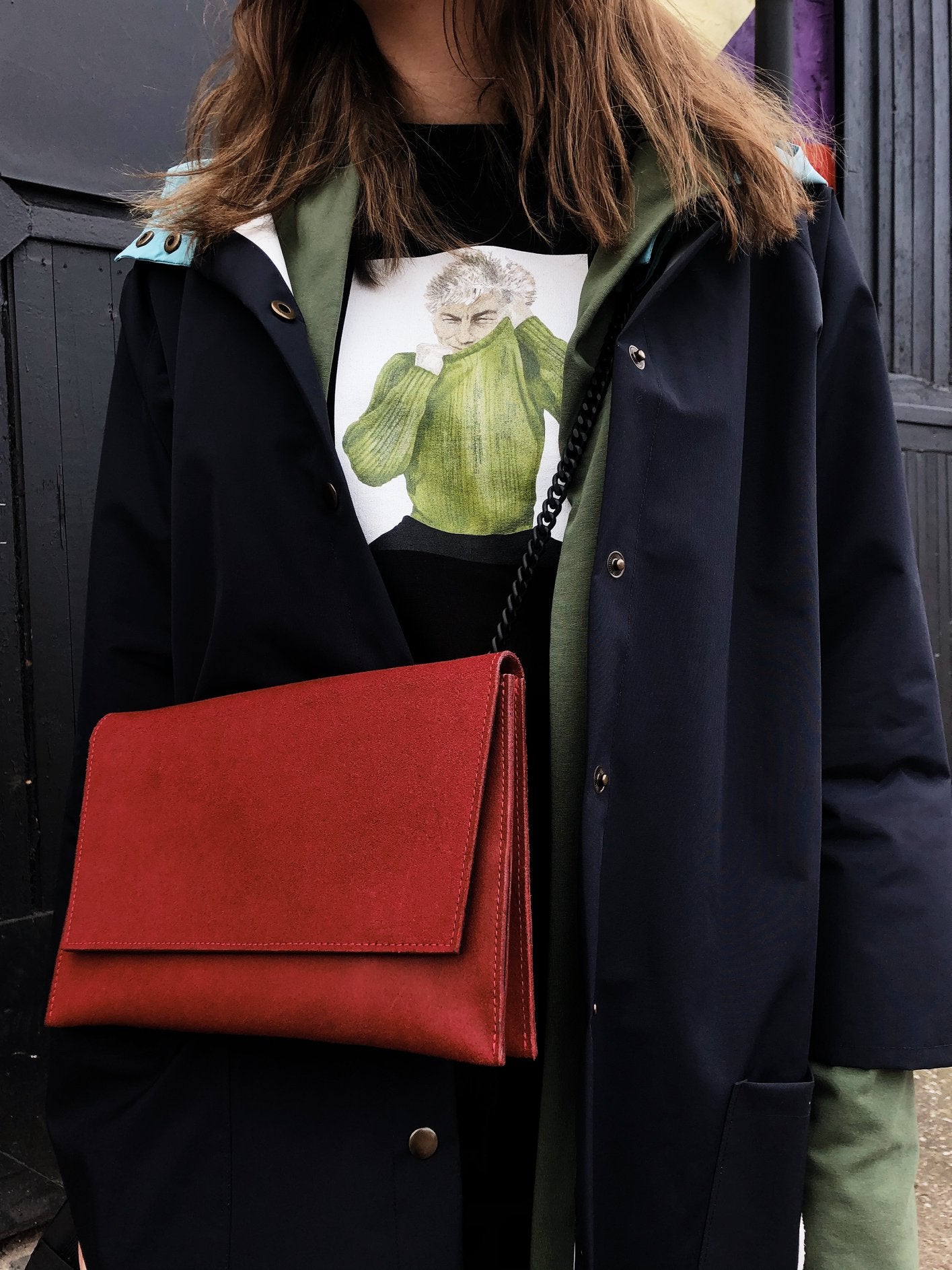 Person wearing a red chain shoulder bag, USMIH Grid design, matte leather with black alloy strap, hand-made in Latvia.