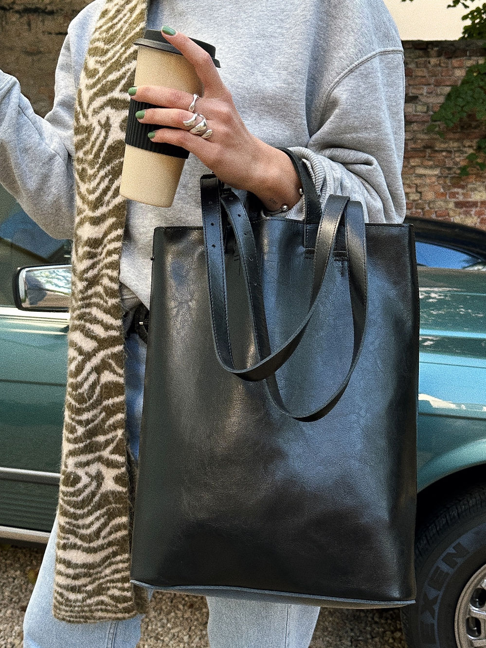 Stylish woman holding a handmade black structured tote bag with USMIH Grid, wearing a gray sweater and zebra print scarf.