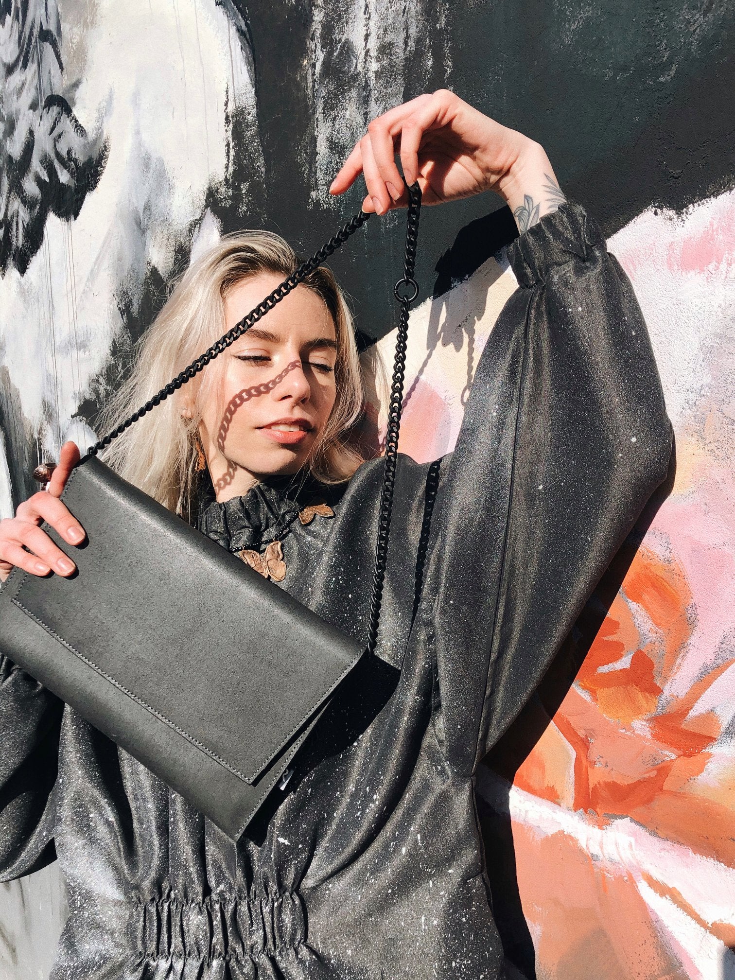 Woman holding black chain shoulder bag with matte leather finish, showcasing USMIH Grid style against a floral mural background.