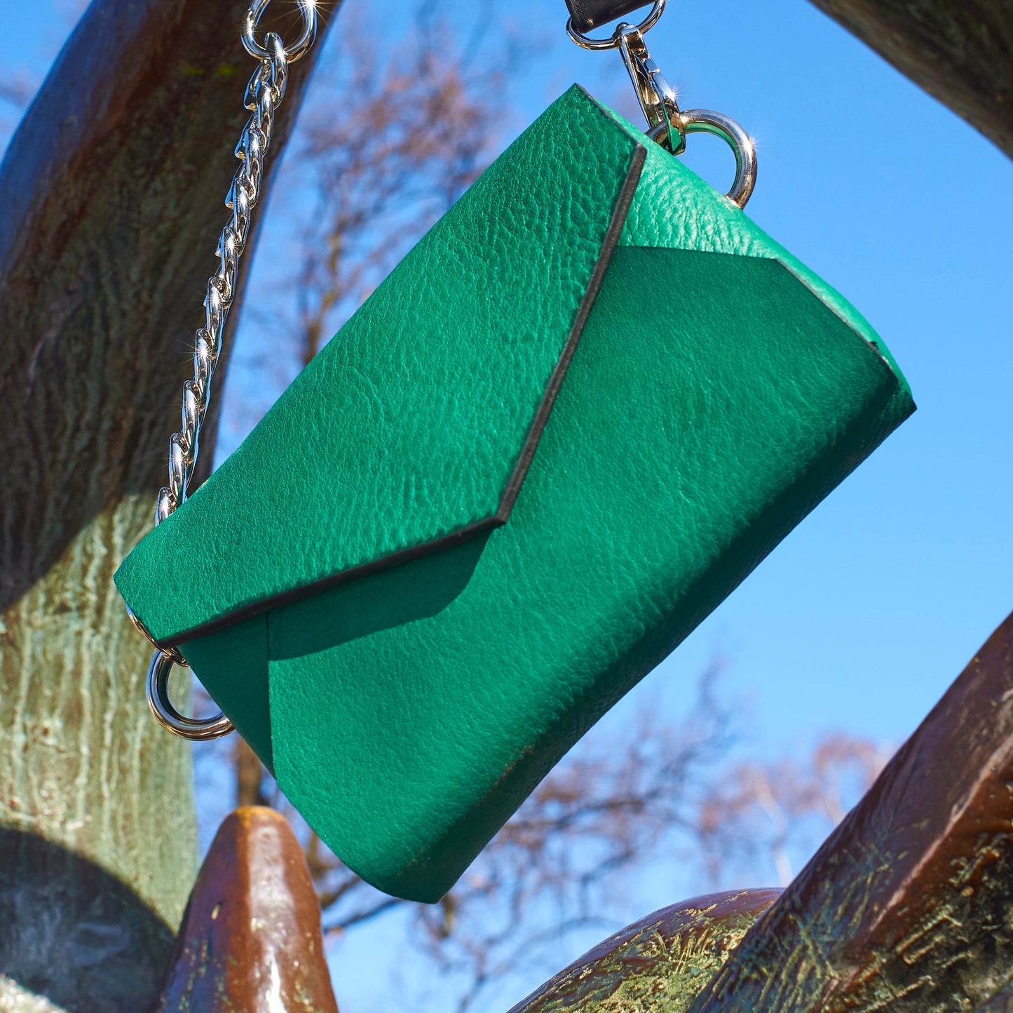 Green handmade leather envelope bag with silver chain hanging outdoors, available on USMIH Grid, buy with card or cryptocurrency.