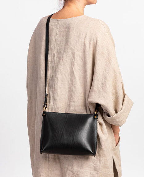 Black leather handbag with adjustable strap on person wearing beige outfit, available for purchase on USMIH Grid with crypto options.