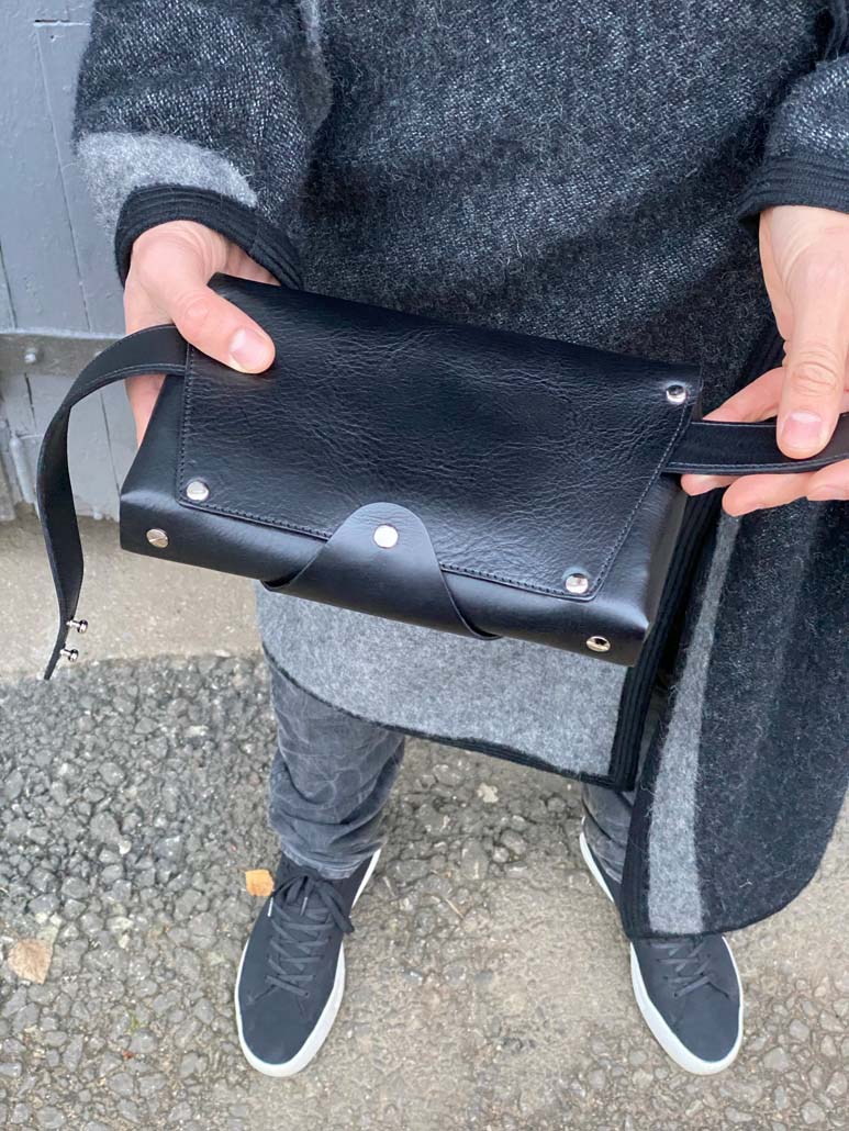 Black leather fanny bag/shoulder bag held by person, available on USMIH Grid, a prime online marketplace for European brands.