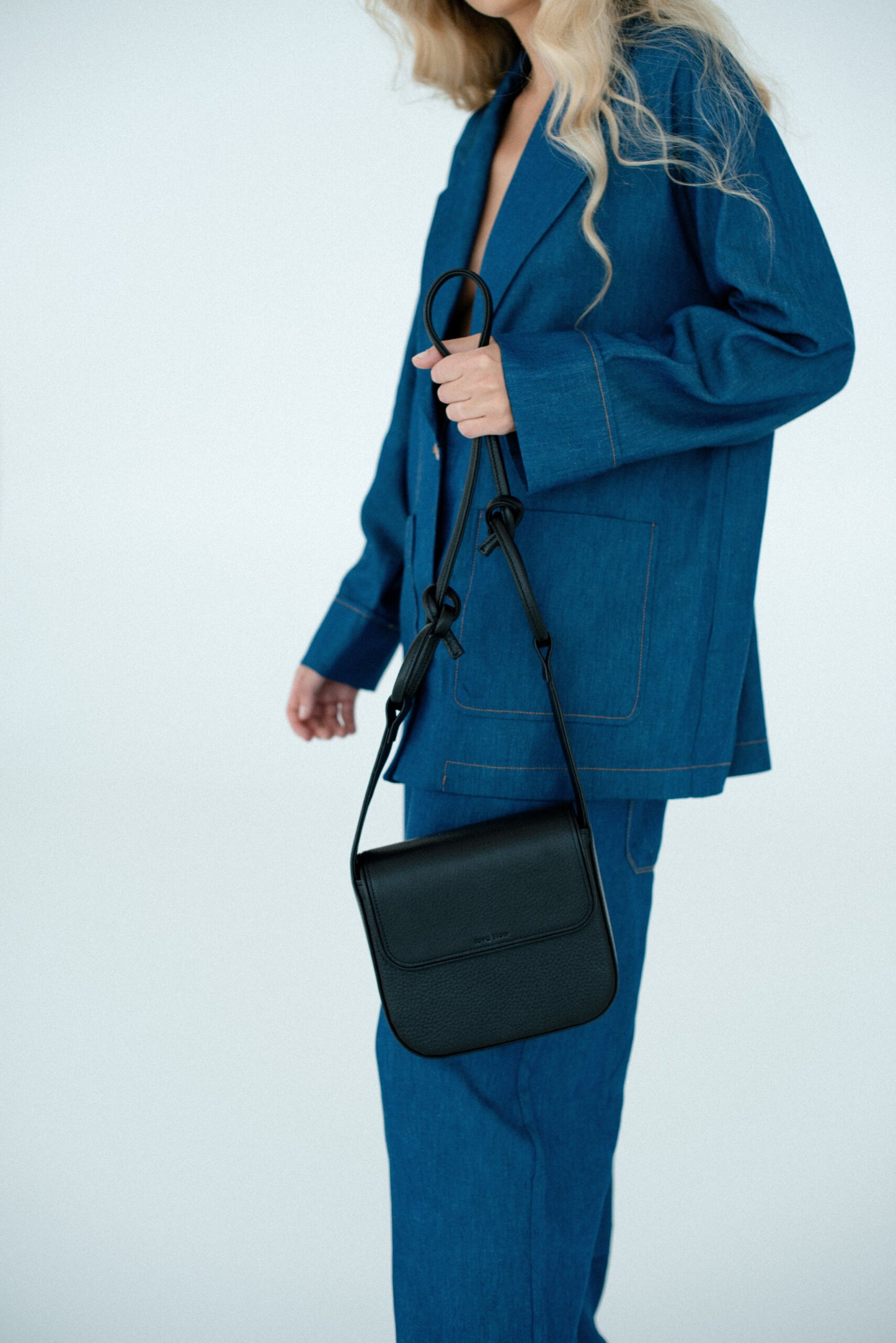 Minimalist black MUSA crossbody bag with adjustable strap, held by person in blue suit, perfect luxury gift idea | Find USMIH.