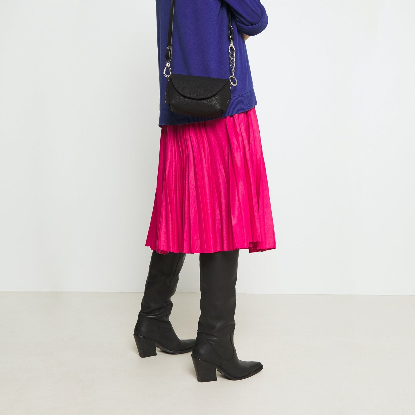 Woman carrying black handmade leather shoulder bag, styled with pink skirt and boots, available on USMIH Grid with card and crypto payments.