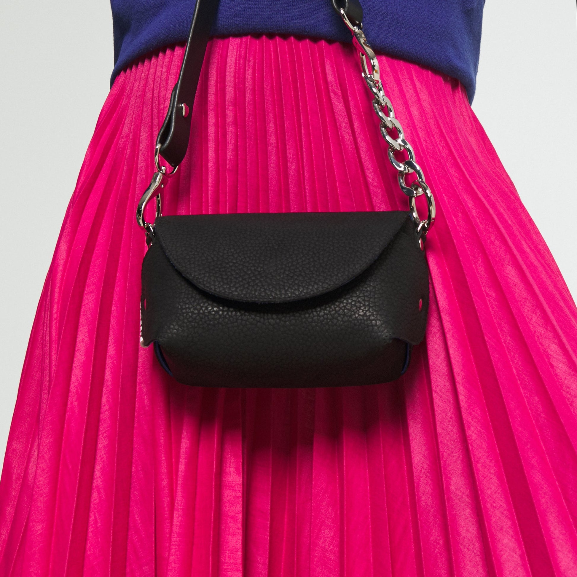 Black handmade leather shoulder bag with silver hardware and adjustable strap, styled with a vibrant pink skirt, USMIH Grid.